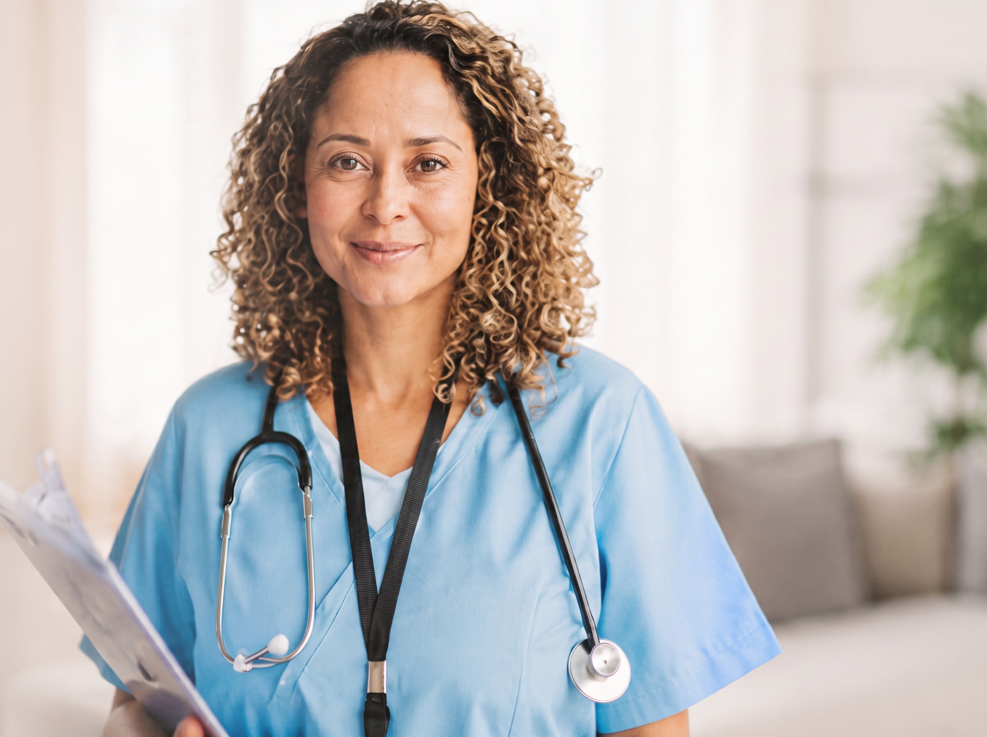 Nurse in blue scrubs smiling while holding a clipboard