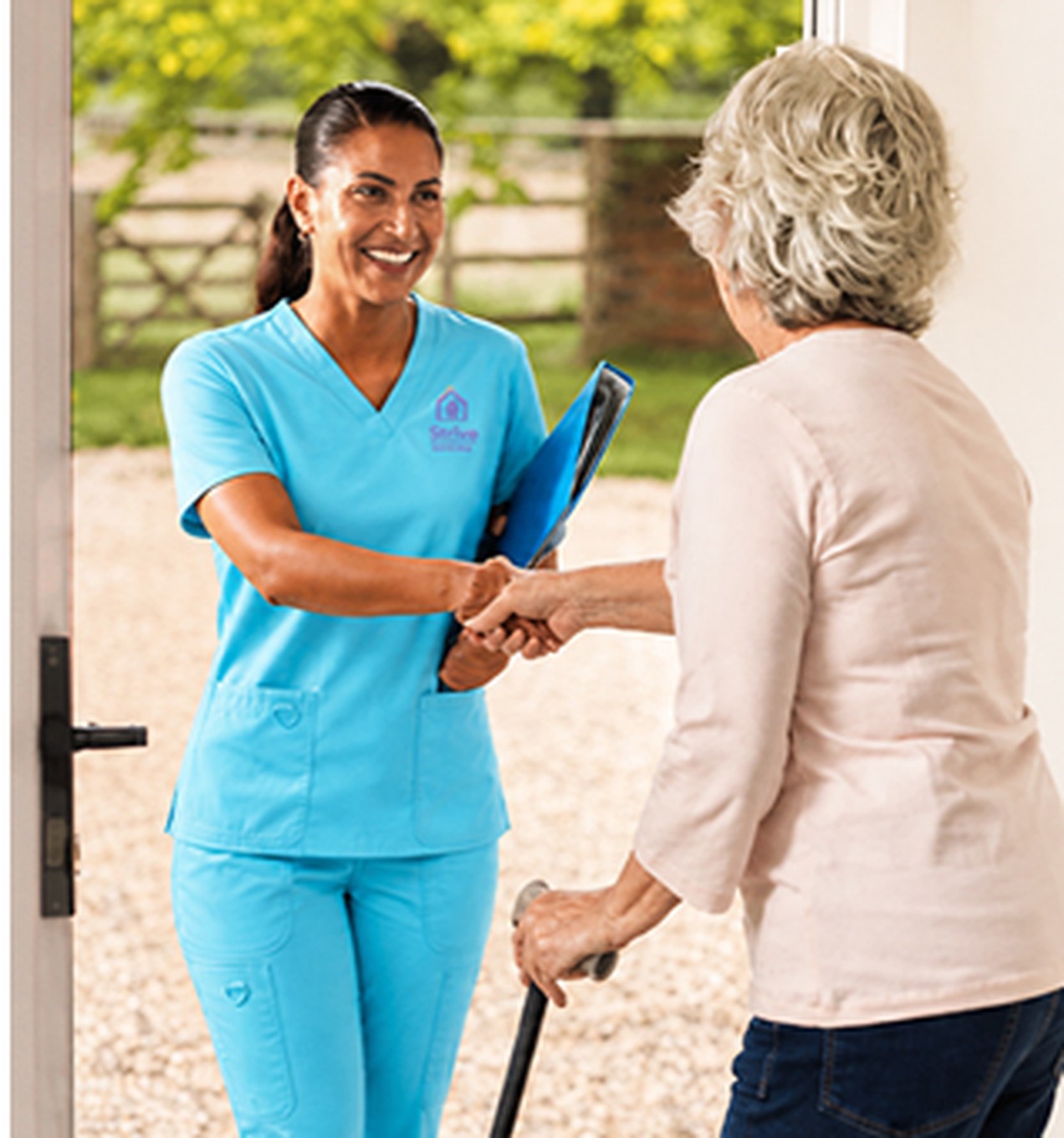 Nurse in turquoise scrubs greeting a client at her front door